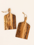 Two wooden serving boards with engraved botanical leaf patterns and hanging loops, displayed on a light cream background.